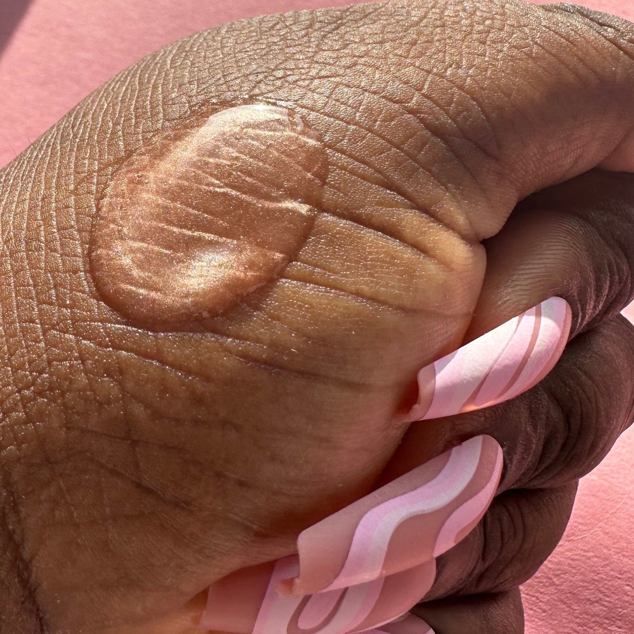 Hand with brown skin, pink and white swirl pattern nails, pink background