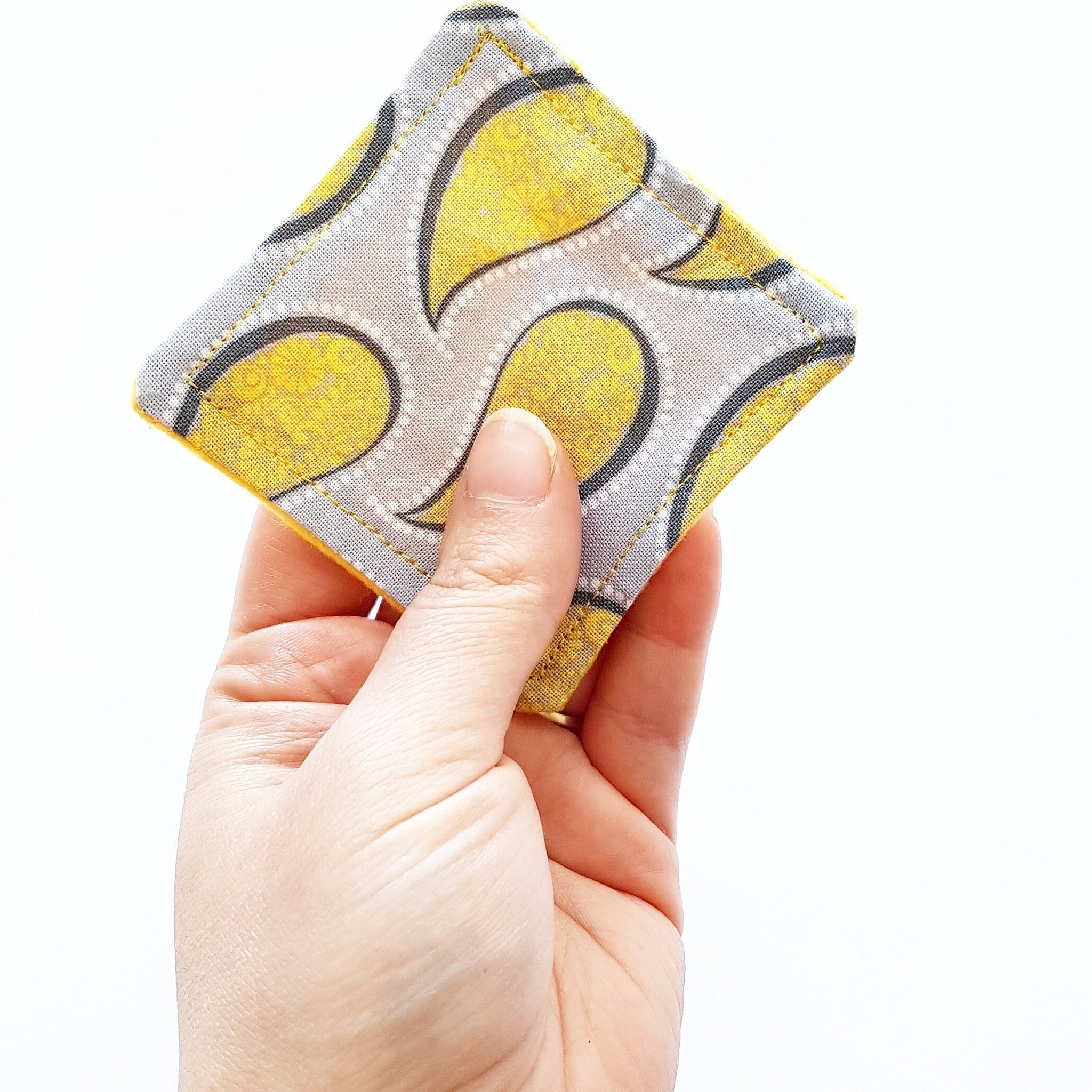 Square fabric coaster with yellow paisley pattern and gray trim, held in hand