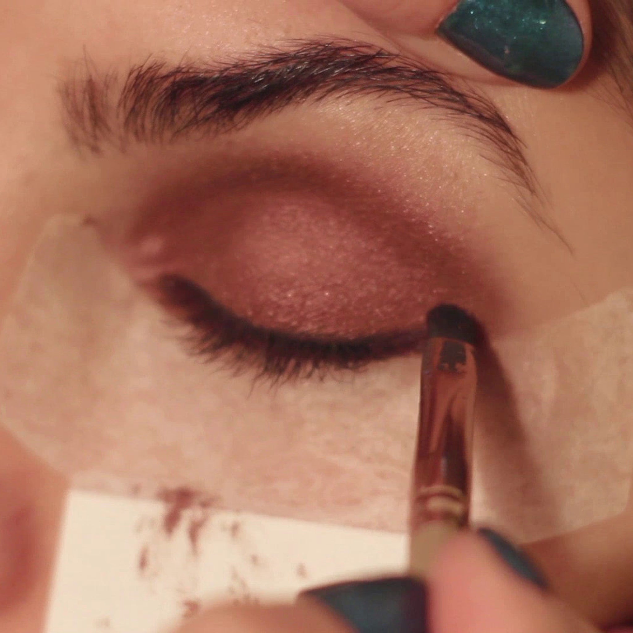 Eyeshadow application with brown eyeshadow, brush, and green nail polish on fingers