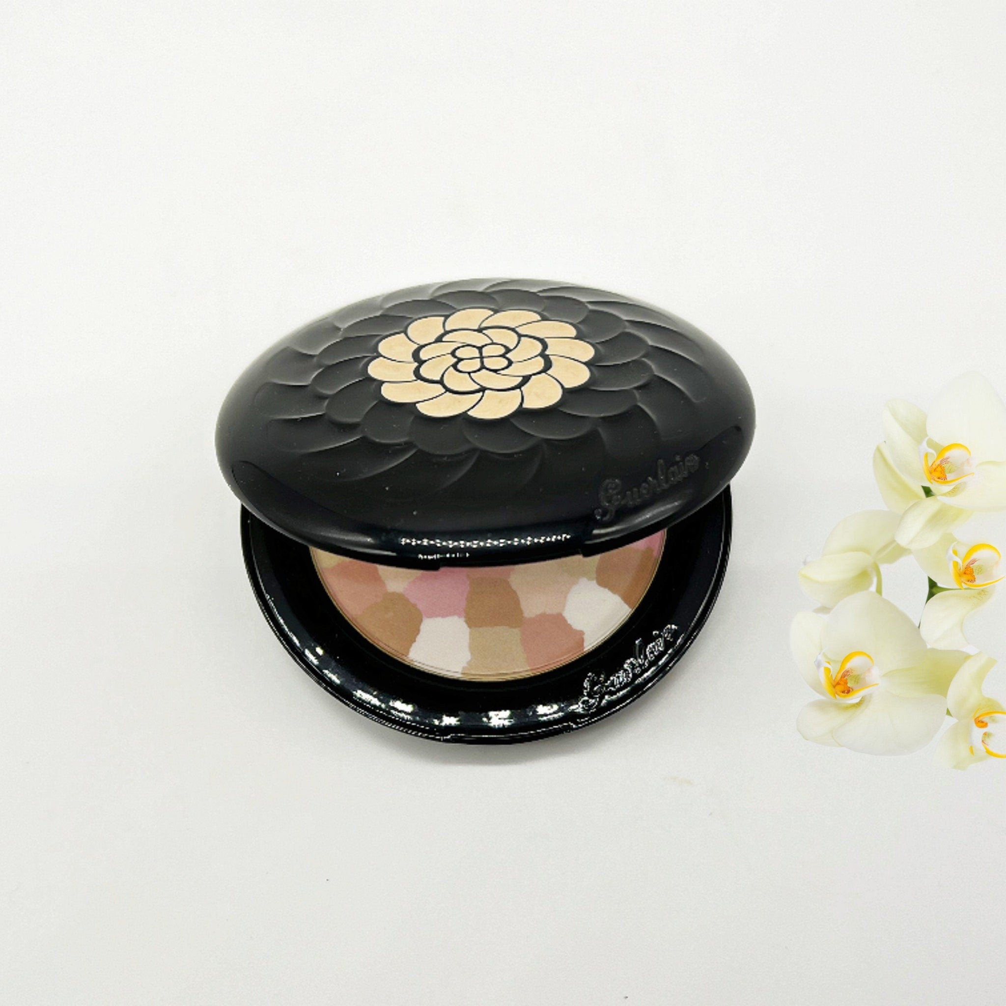 Powder compact, black floral lid, multi-color powder, Guerlain brand name visible