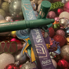 Shadow Stix makeup in green and purple packaging, with Alice in Wonderland character sticker and Christmas ornaments