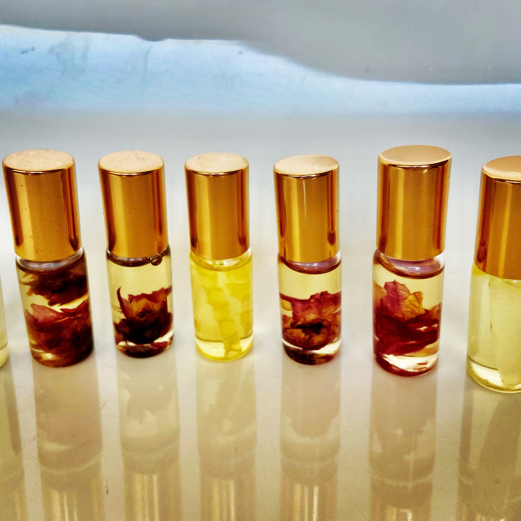 Lip gloss bottles with gold caps, clear glass, and floral inclusions