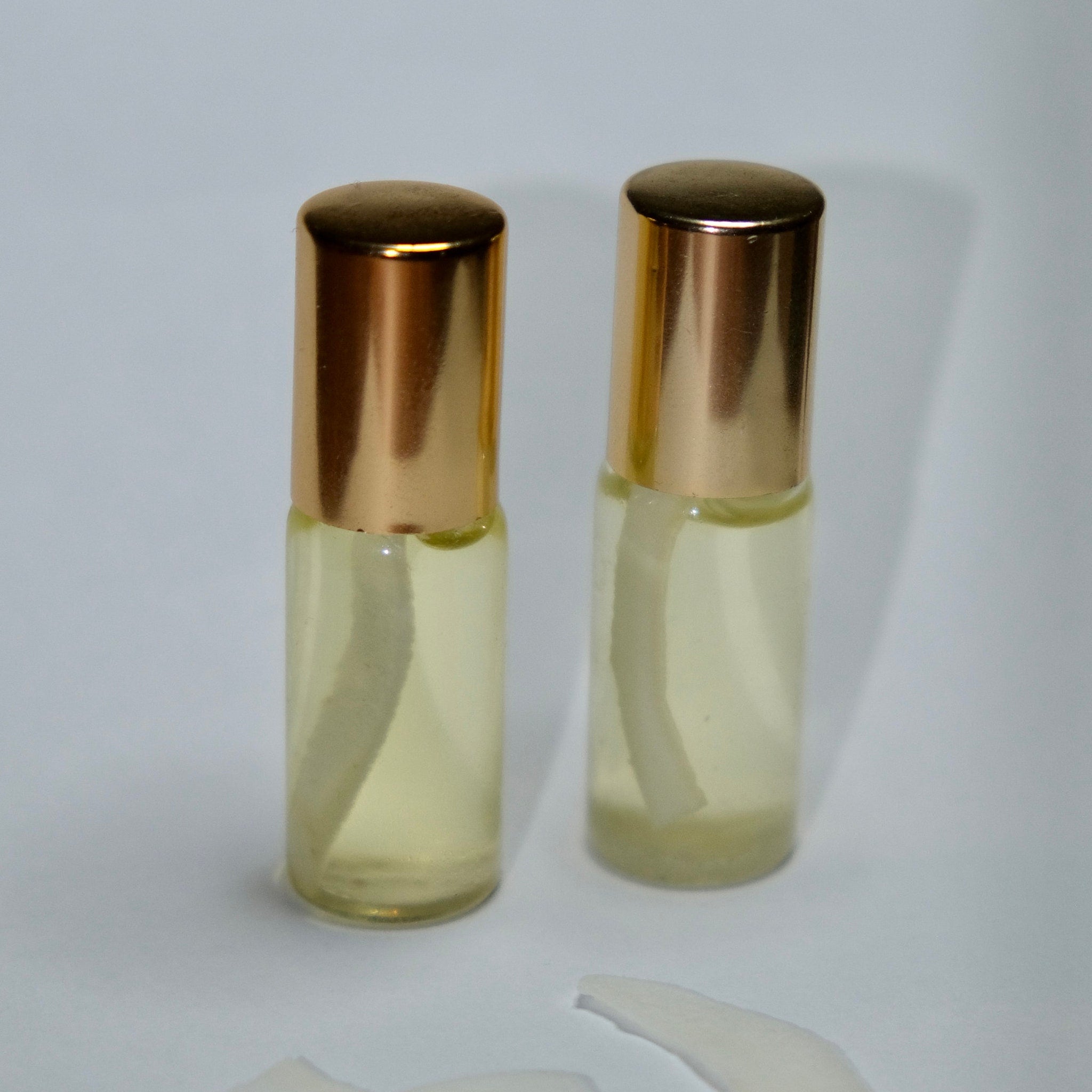 Perfume bottles with gold caps, clear glass, and yellow liquid inside on white surface