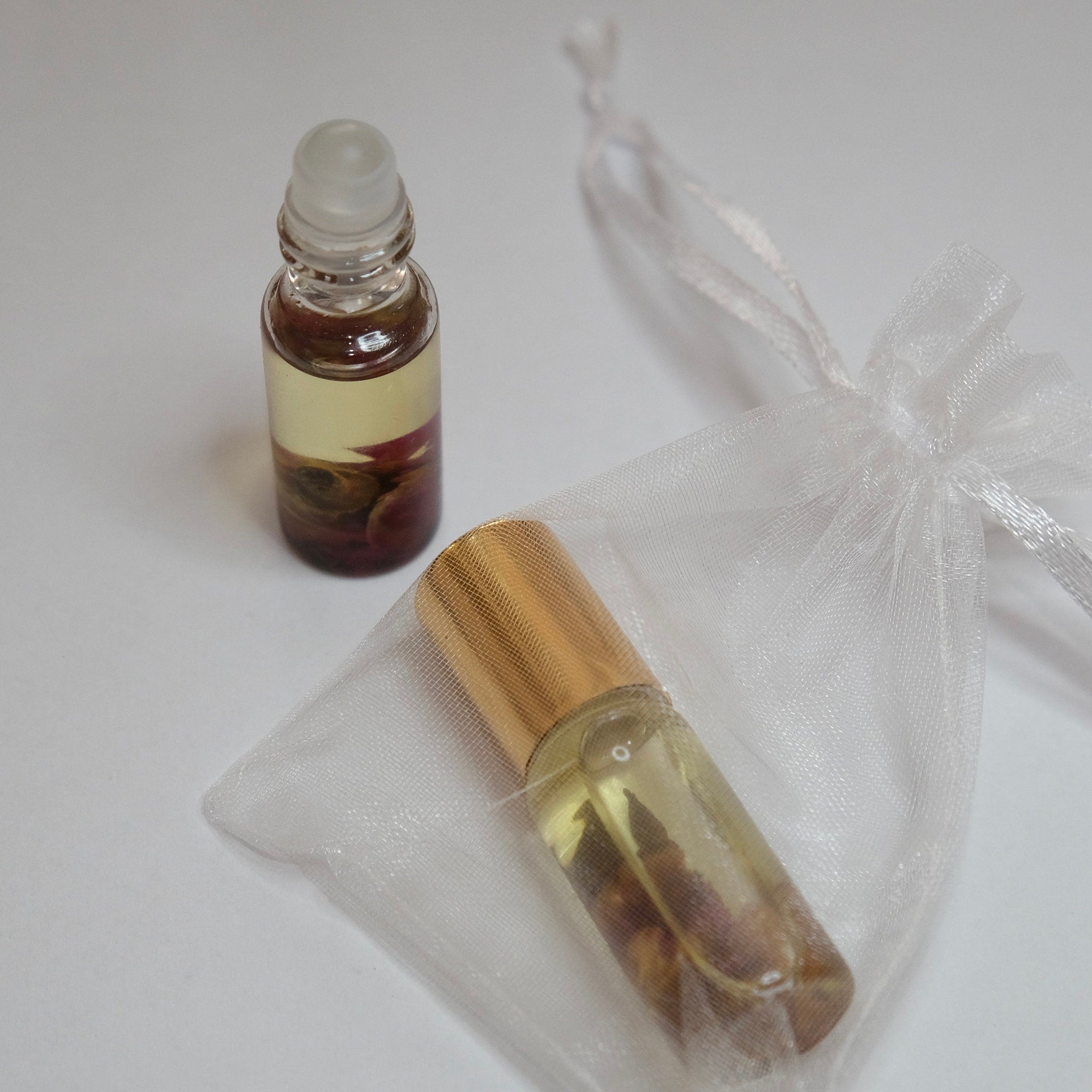 Roller bottle with gold cap, clear glass, and white organza bag on white surface