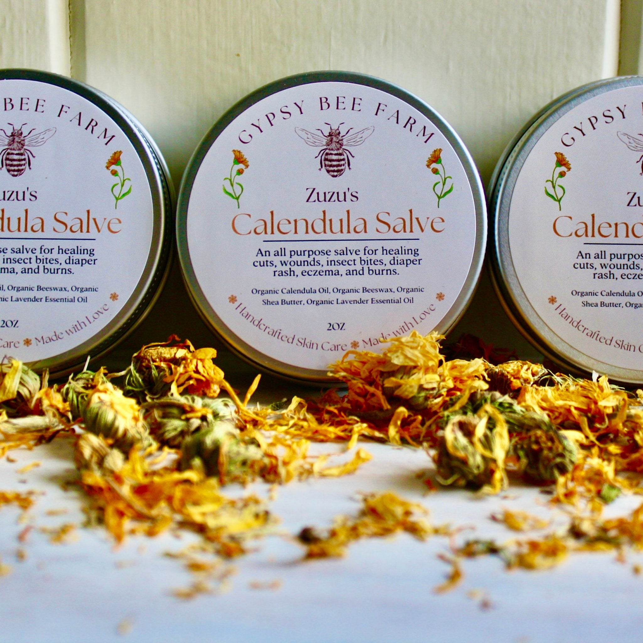Calendula salve in metal tins with white labels, Gypsy Bee Farm branding, and dried flowers