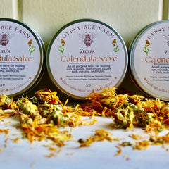 Calendula salve in metal tins with white labels, Gypsy Bee Farm branding, and dried flowers