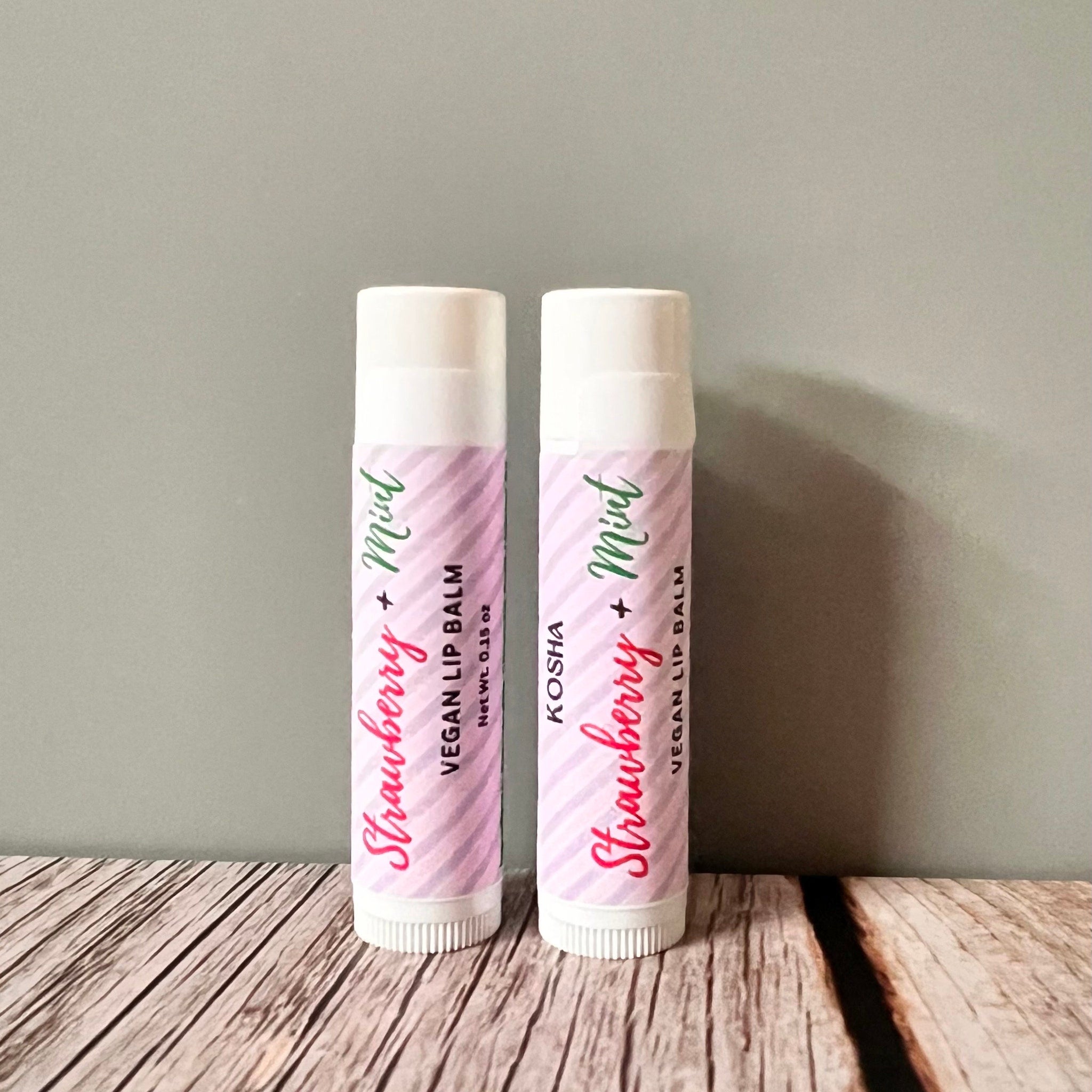 Lip balm tubes with pink and white striped pattern, brand name Kosha visible, on wooden surface