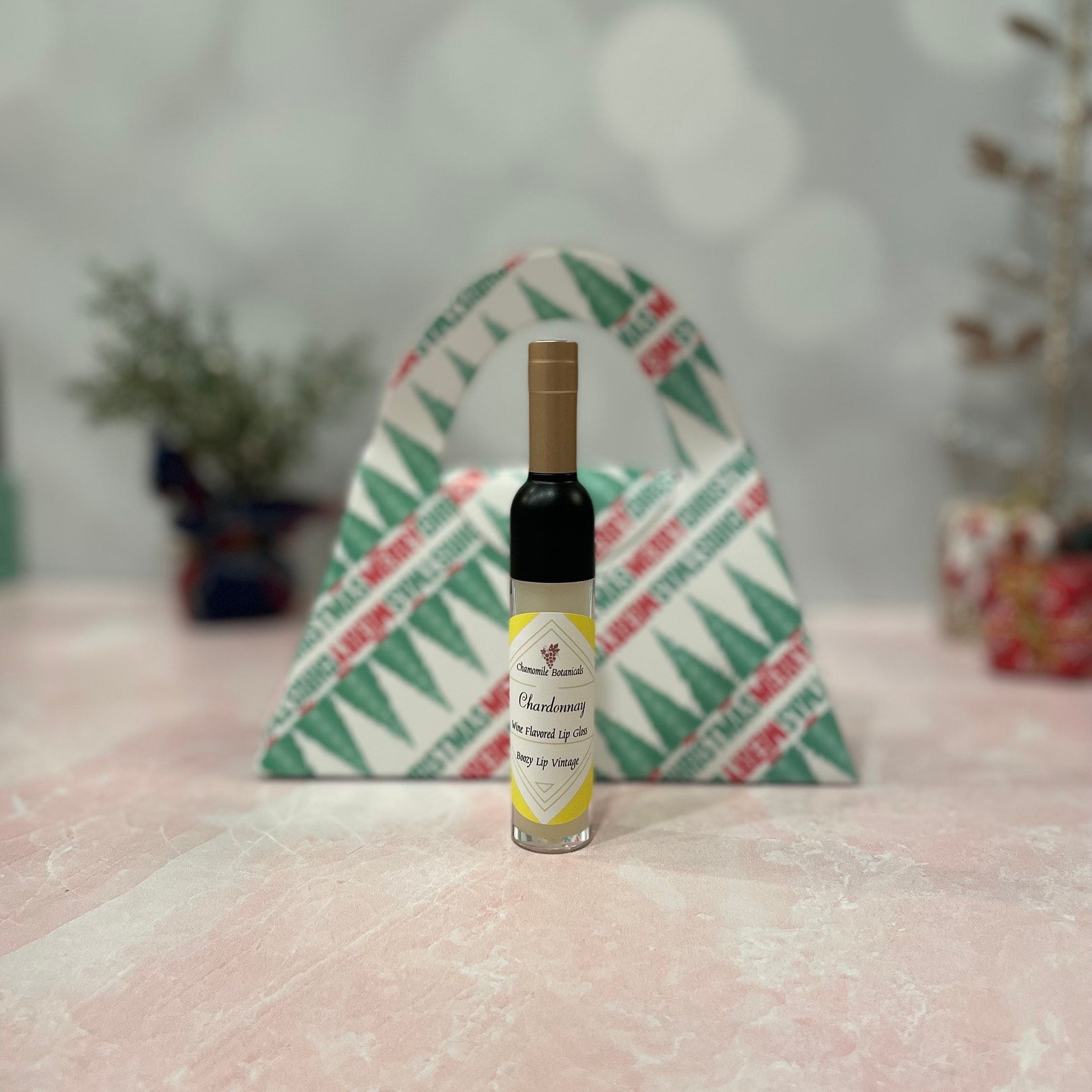Lip gloss bottle with black, gold, and clear glass, with label "Chardonnay" in front of Christmas gift bag.