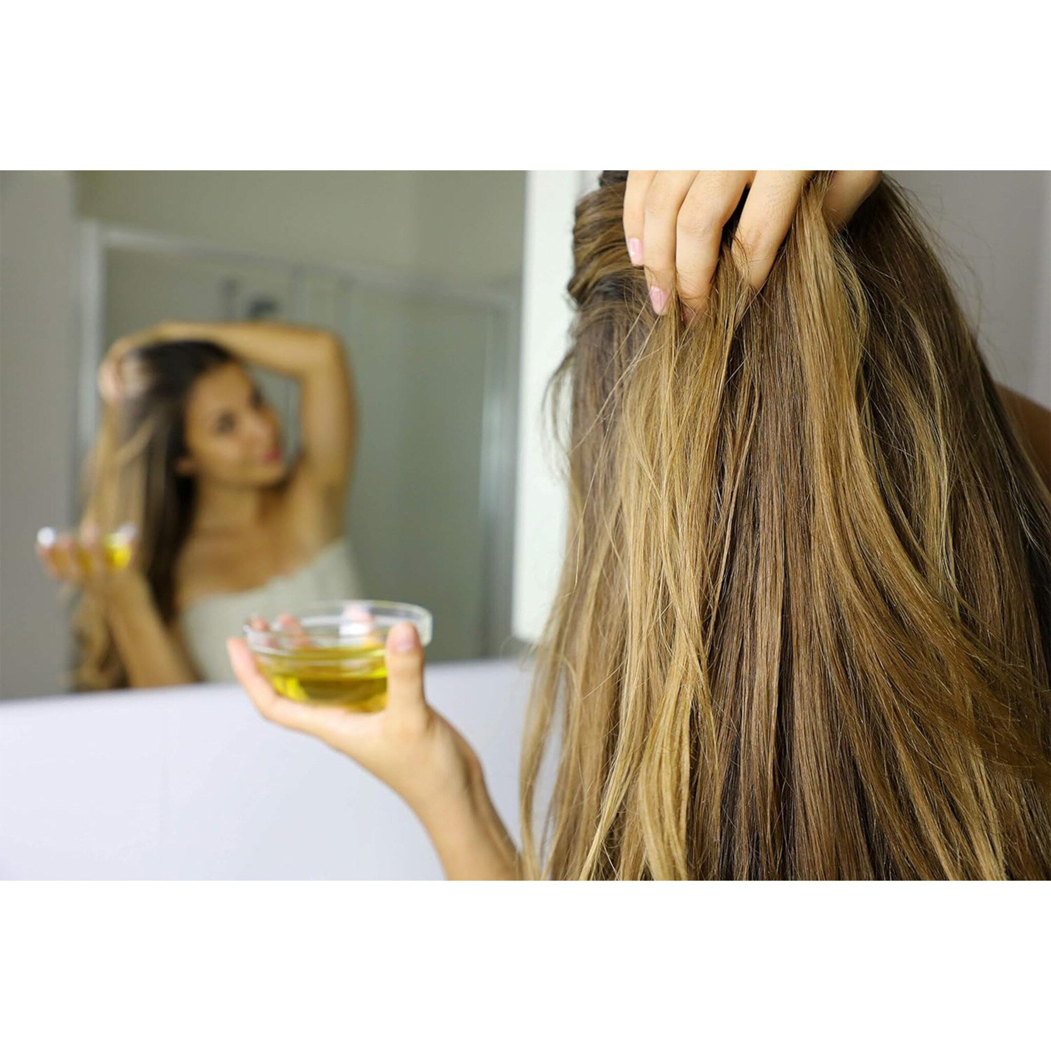 Hair oil application, blonde and brown hair with hand holding glass bowl of oil in bathroom setting