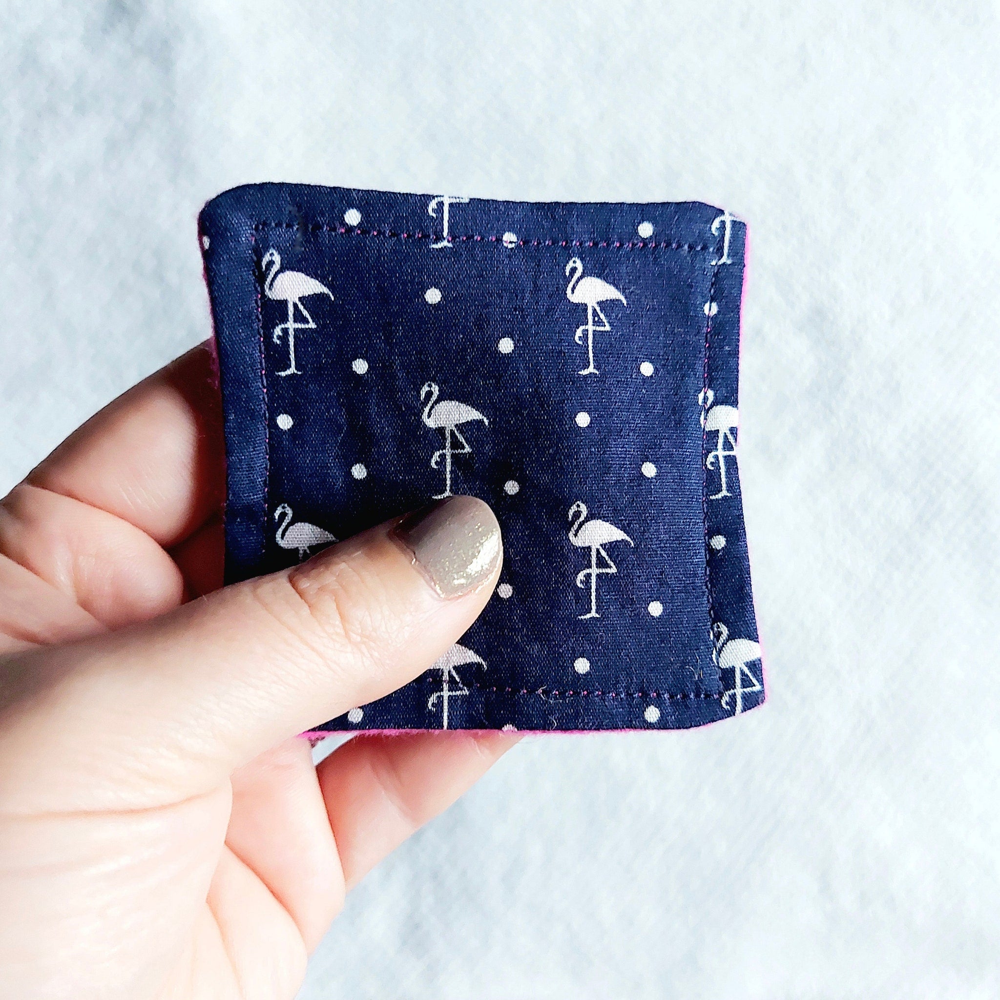 Makeup remover pad, dark blue flamingo print fabric, held in hand