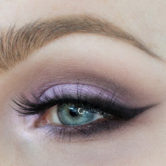 Close-up of a makeup brush applying soft pastel purple lavender eyeshadow to eyelid for a subtle shimmer look.