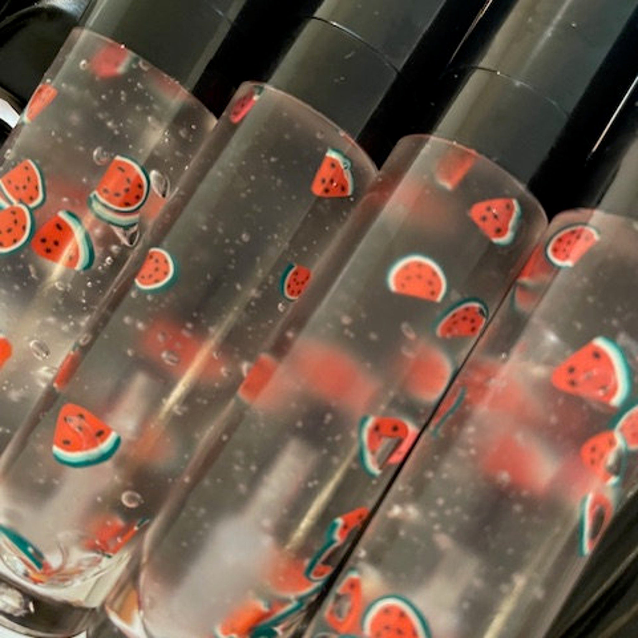 Lip gloss tubes with watermelon slice pattern, clear liquid, and black caps