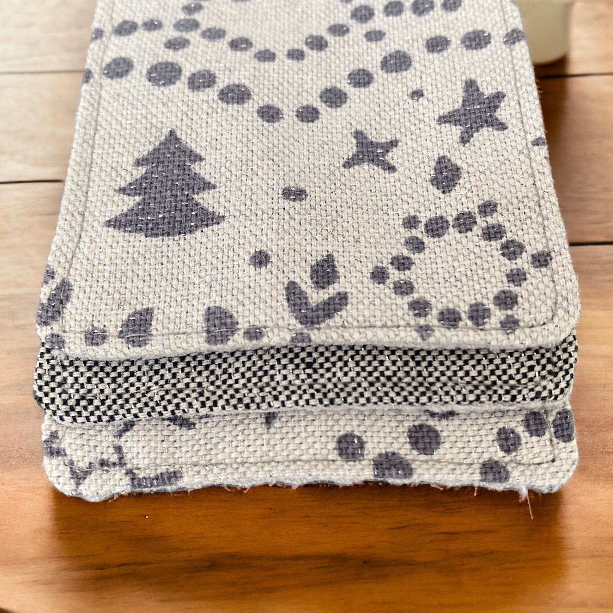 Coasters with gray tree and star pattern on off-white woven material, stacked on wood surface
