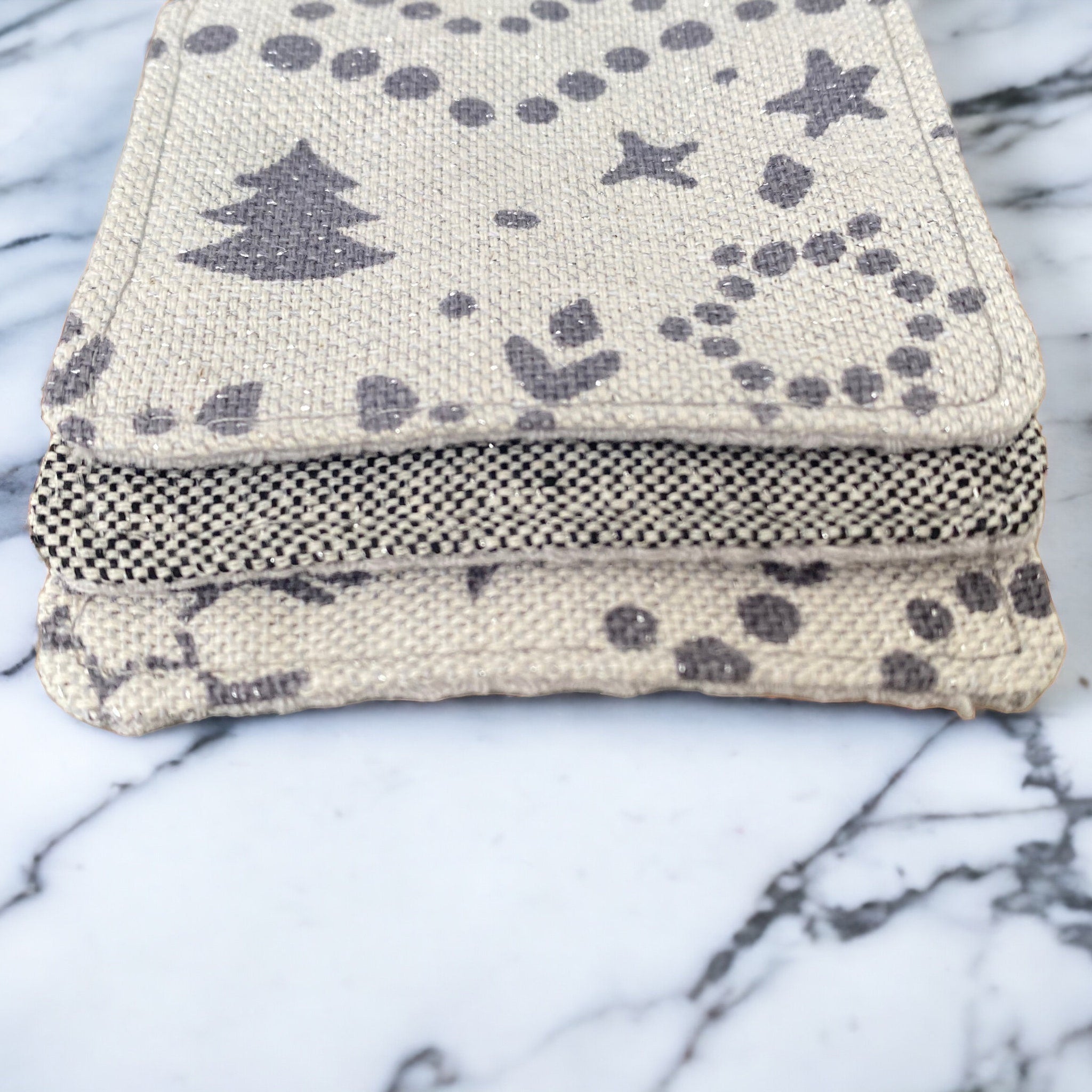 Cloth napkins with gray tree and dot patterns, stacked with black and white checkered napkin on marble surface