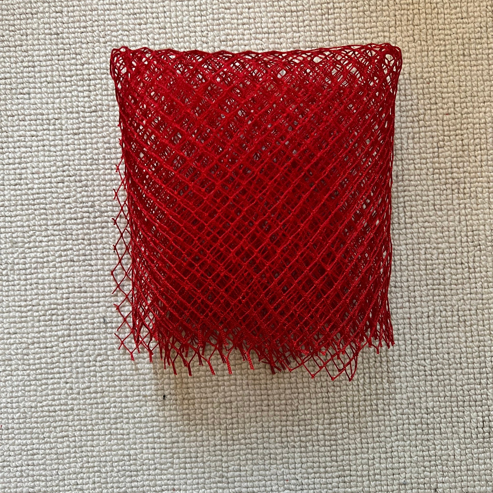 Red mesh fabric with diamond pattern and fringed edge on textured surface