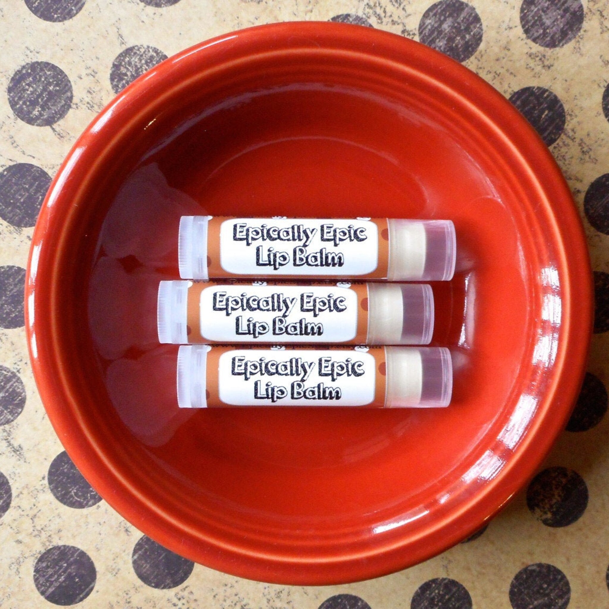 Lip balm tubes with brown, white, and clear plastic, inside a red bowl, with "Epically Epic" text visible