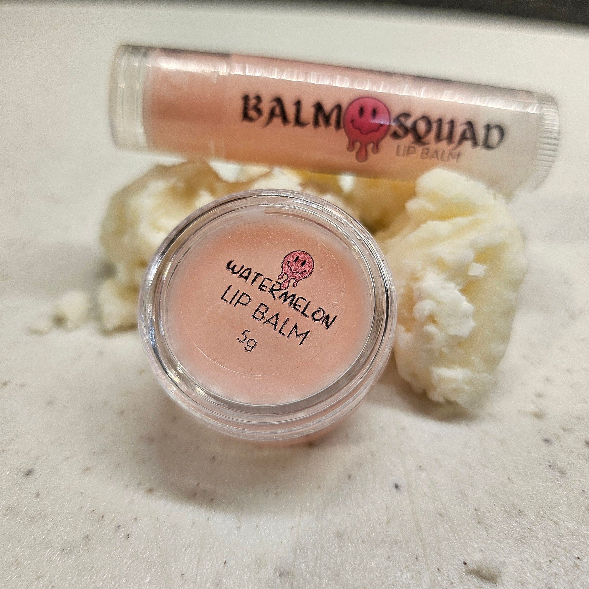 Lip balm with pink color and clear container, "Watermelon" text, and "Balm Squad" branding visible