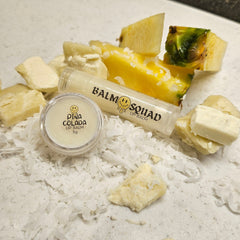 Lip balm tube and jar with white and clear packaging, pineapple and coconut flakes around it