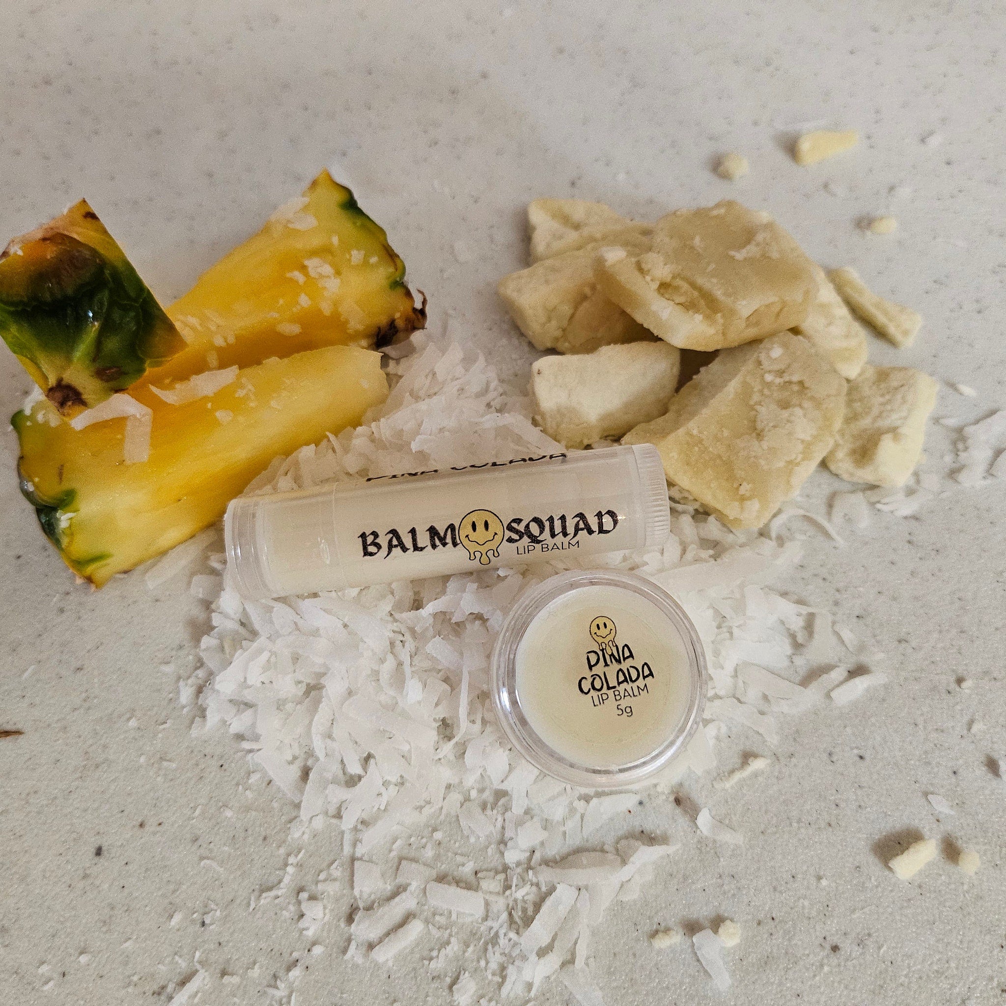 Lip balm with white tube, "Balm Squad" text, and pineapple slices on white surface