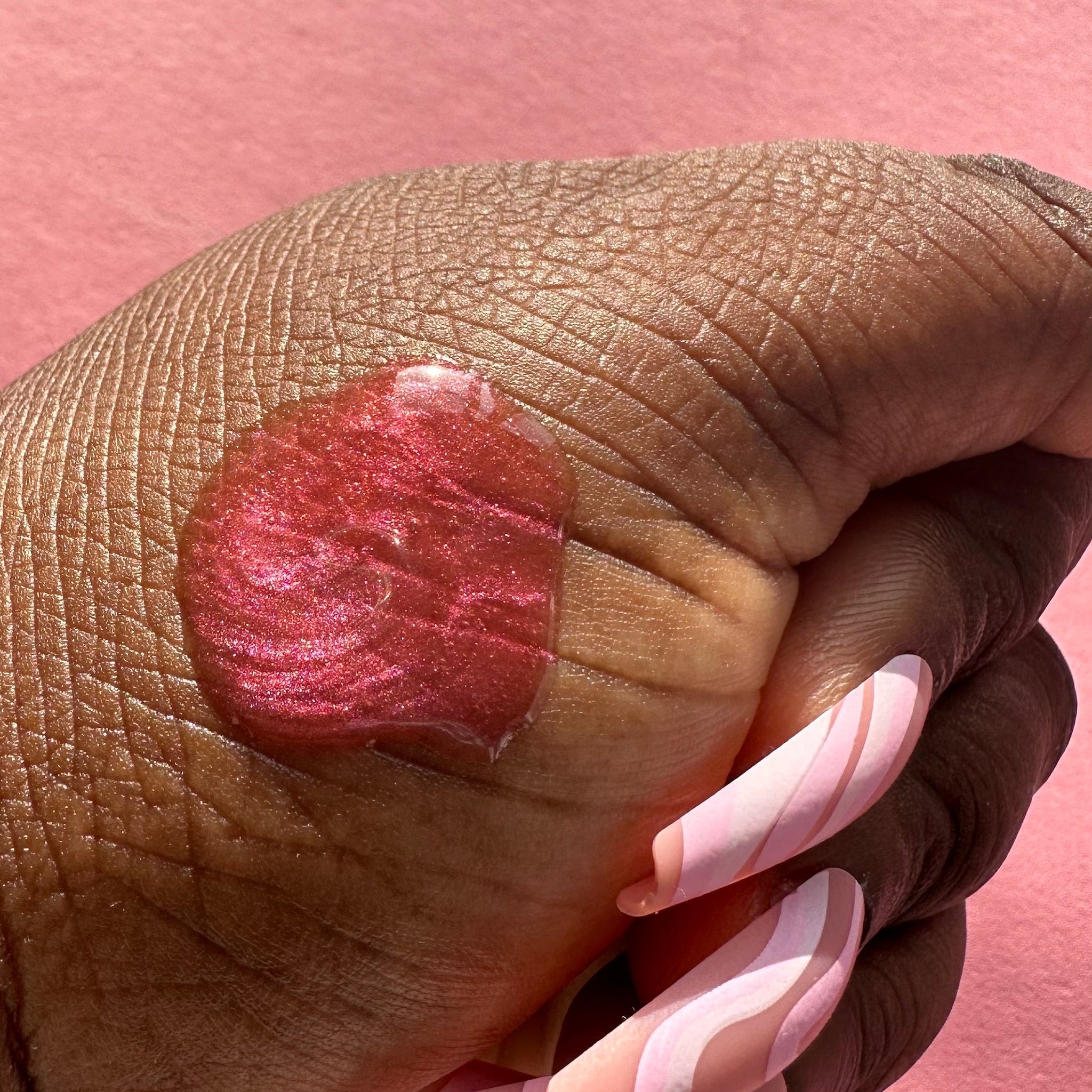 Lip gloss in red with shimmer, applied to skin, with pink and white swirl nails