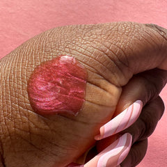 Lip gloss in red with shimmer, applied to skin, with pink and white swirl nails