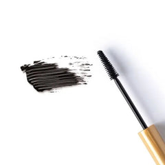 Mascara brush with black bristles and black wand, gold base, and black mascara swatch on white background