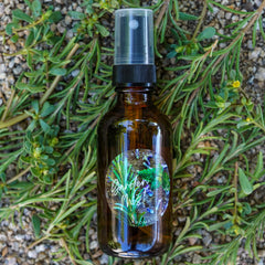 Aromatic spray bottle, brown glass, black pump, clear cap, with "Garden Mist" label, surrounded by green plants