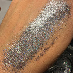 Side view of dark gray holo glitter eyeshadow pan showing reflective sparkle and smooth pressed powder texture