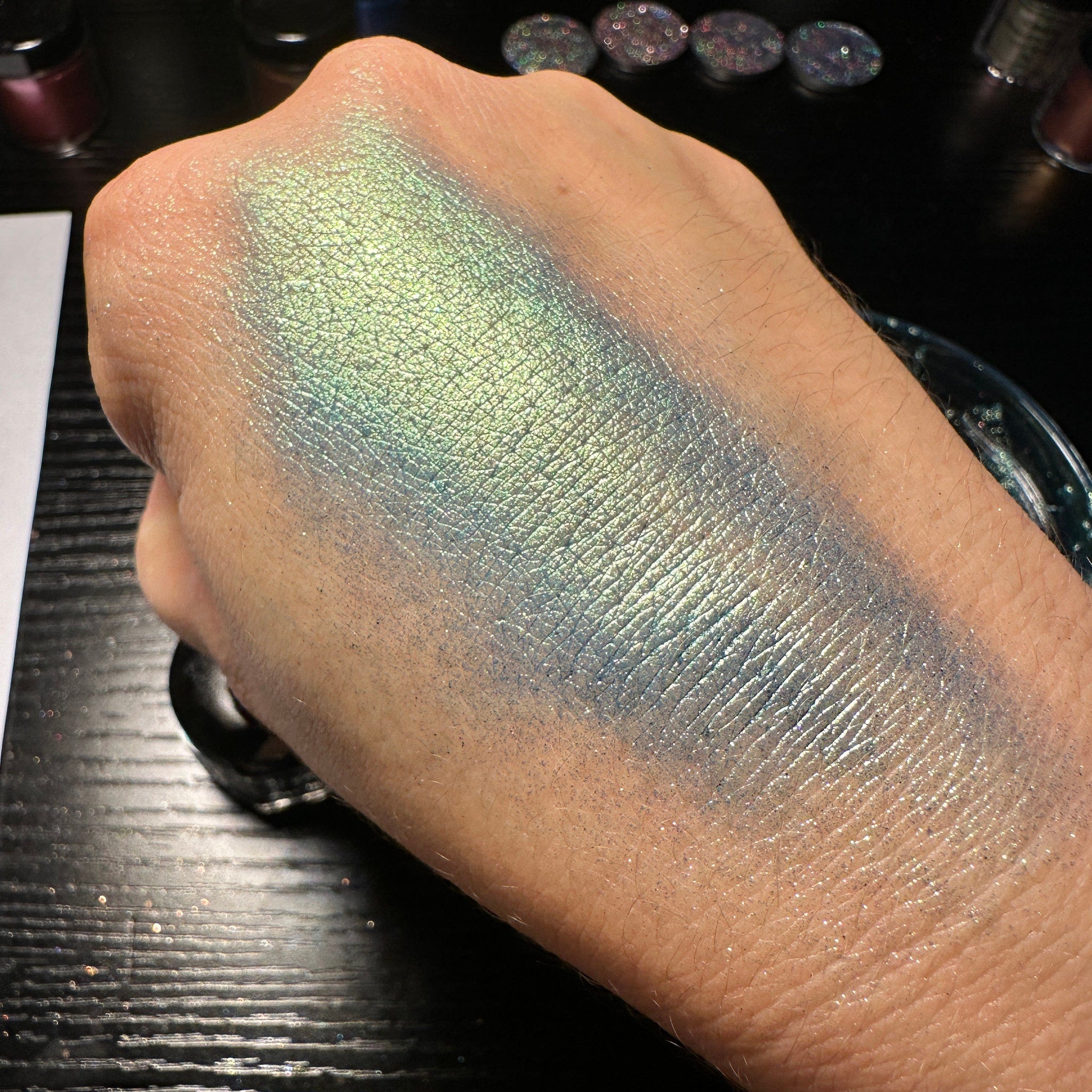 Side view of green duochrome pressed glitter eyeshadow pan showcasing shifting metallic hues