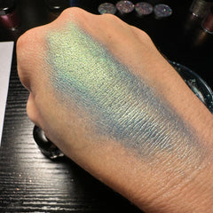 Side view of green duochrome pressed glitter eyeshadow pan showcasing shifting metallic hues