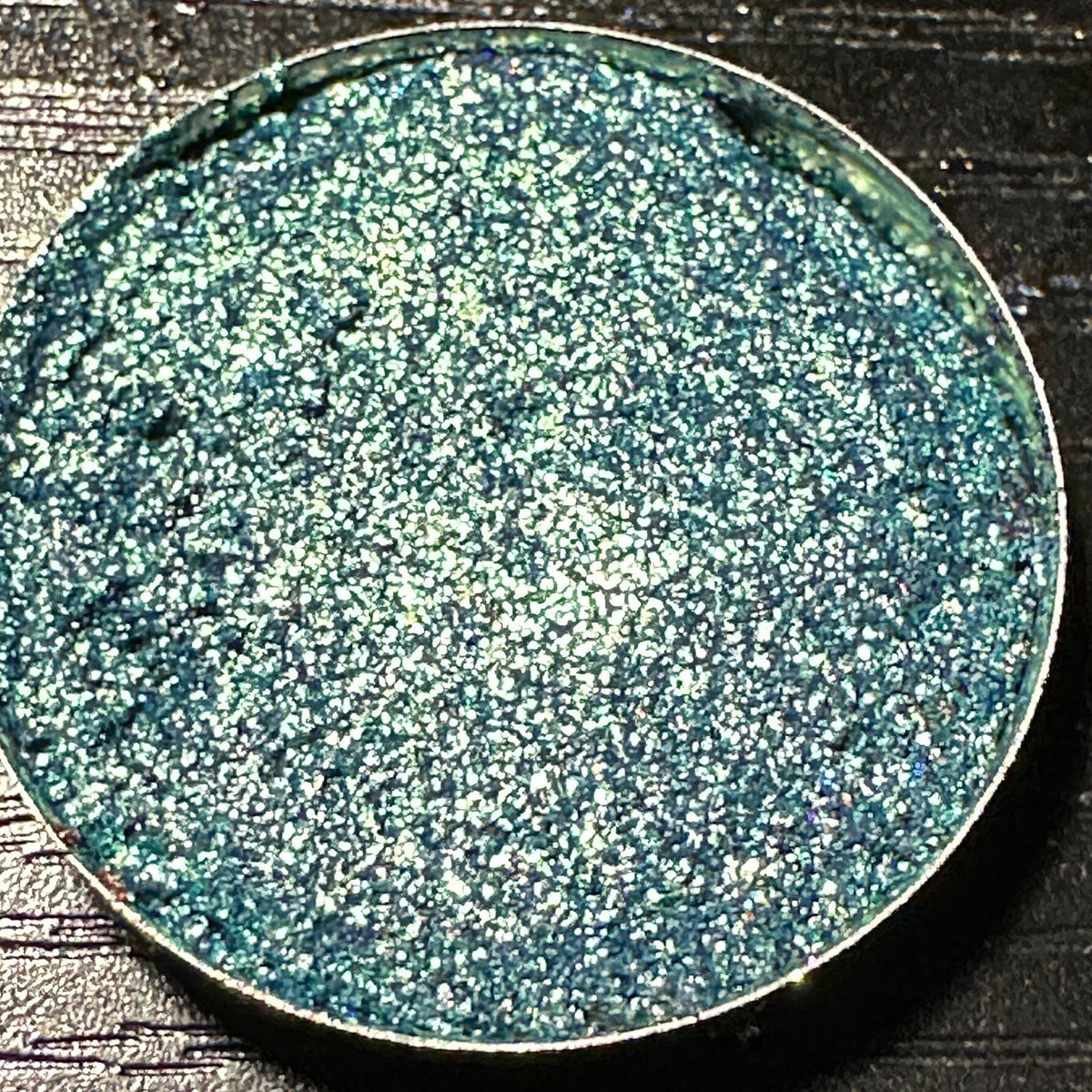 Close-up of green duochrome pressed glitter eyeshadow pan with shimmering color shift effect