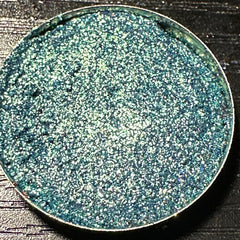 Close-up of green duochrome pressed glitter eyeshadow pan with shimmering color shift effect