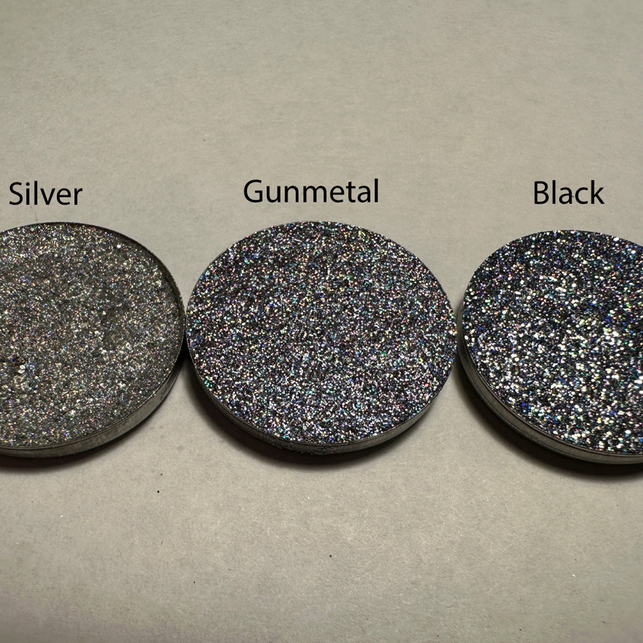 Side view of black holo pressed glitter eyeshadow in 26mm pan showcasing reflective particles