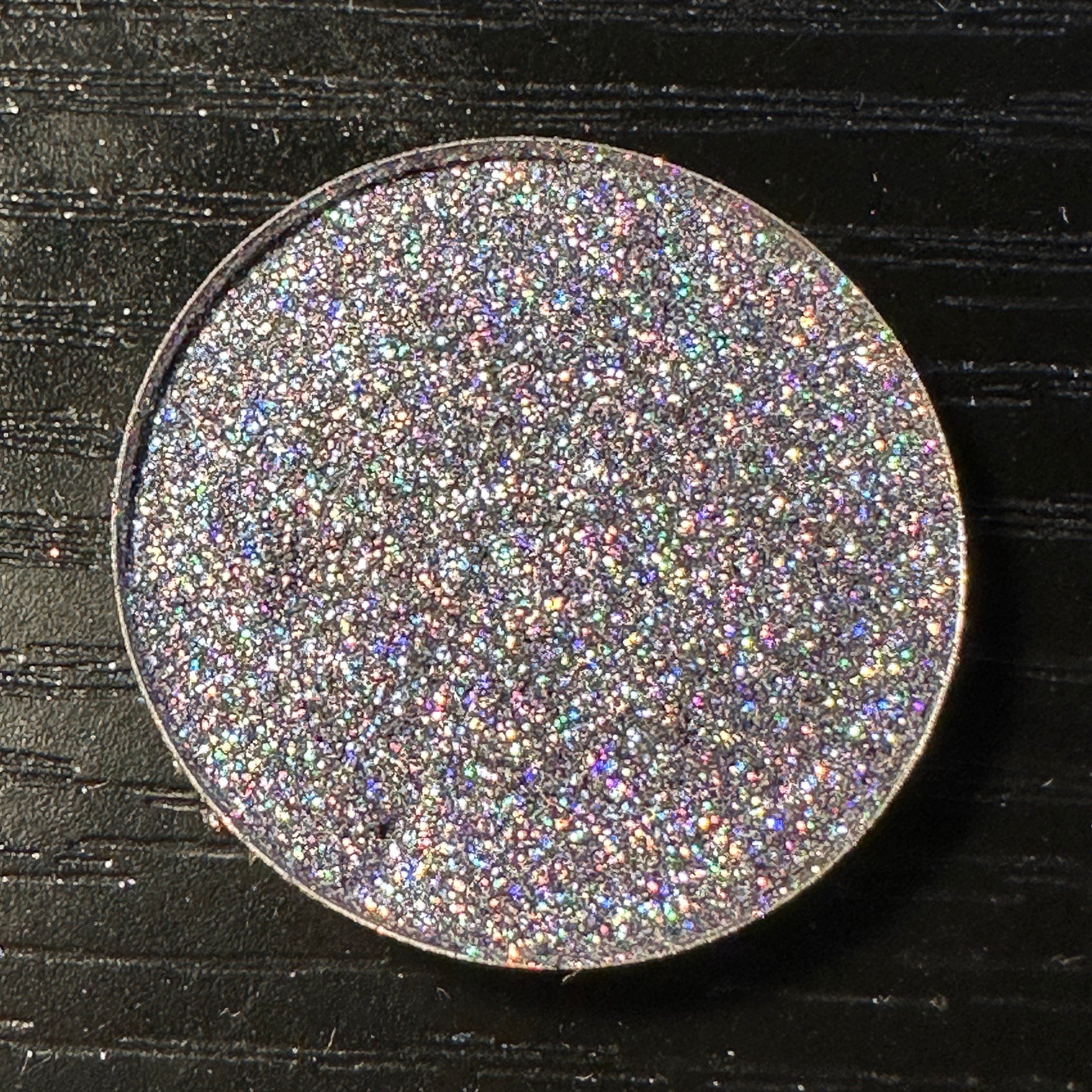 Close-up of black pressed glitter eyeshadow with holographic sparkle in a round 26mm pan