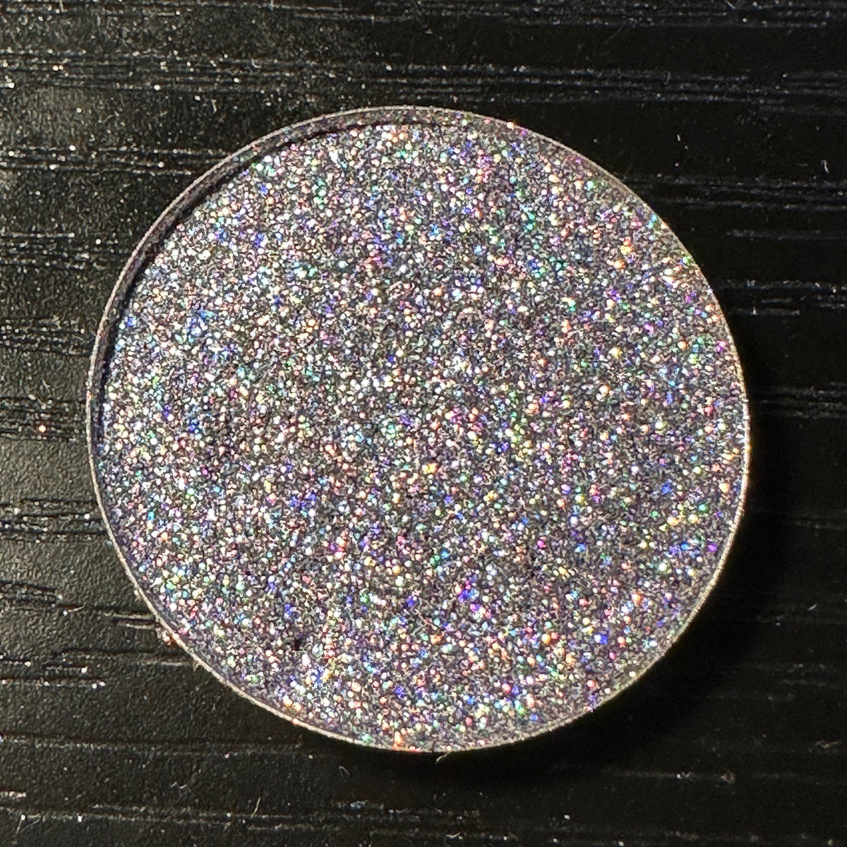 Close-up of black pressed glitter eyeshadow with holographic sparkle in a round 26mm pan