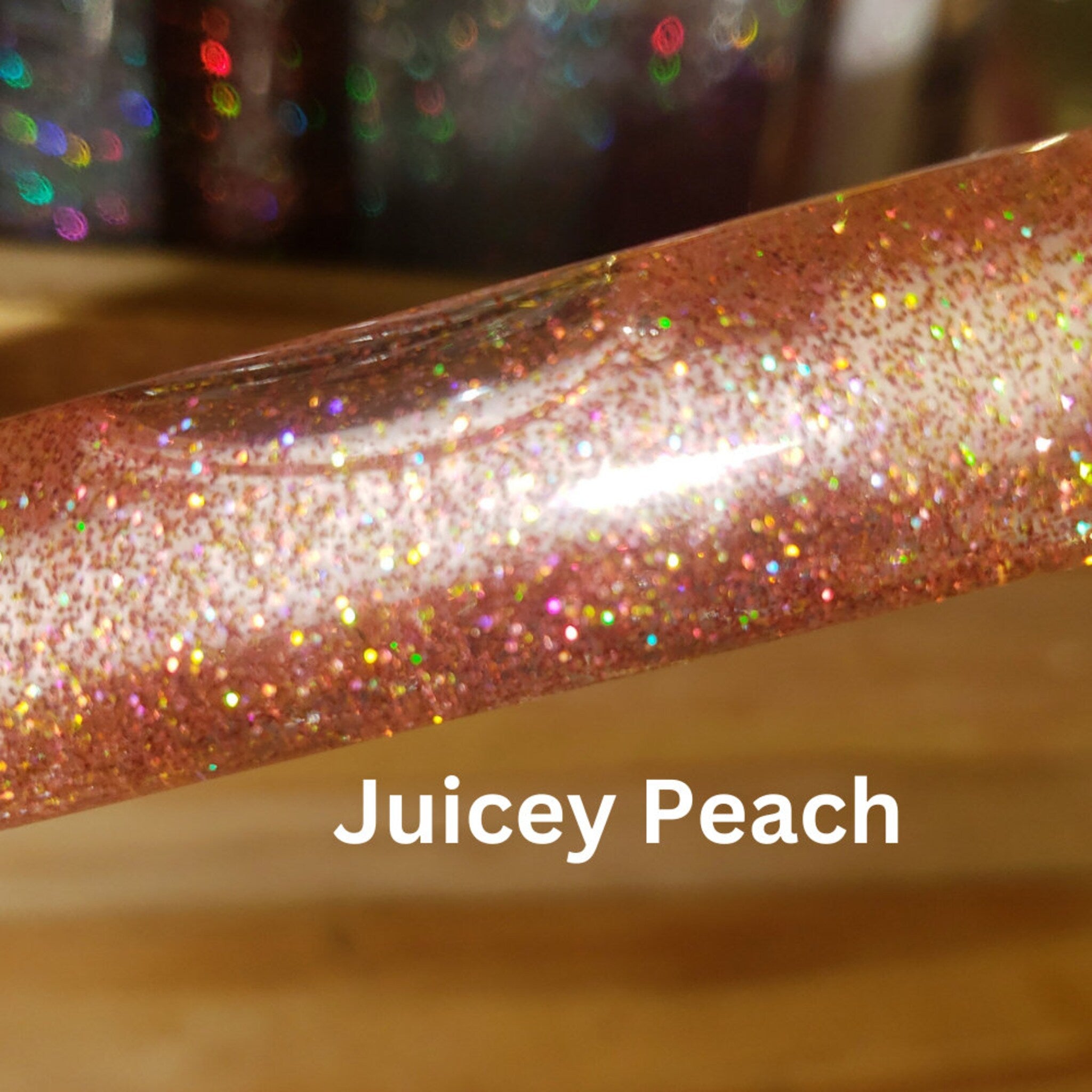 Lip gloss tube with peach glitter and Juicey Peach text, close-up view
