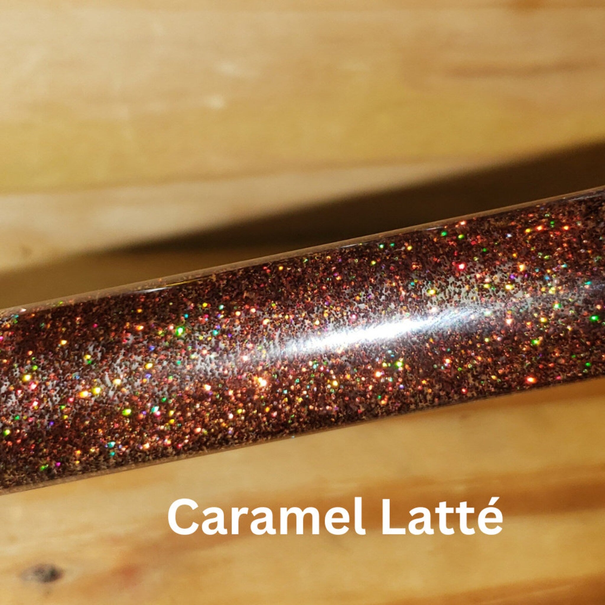 Glittery brown tube with reflective particles and "Caramel Latté" text on wood background