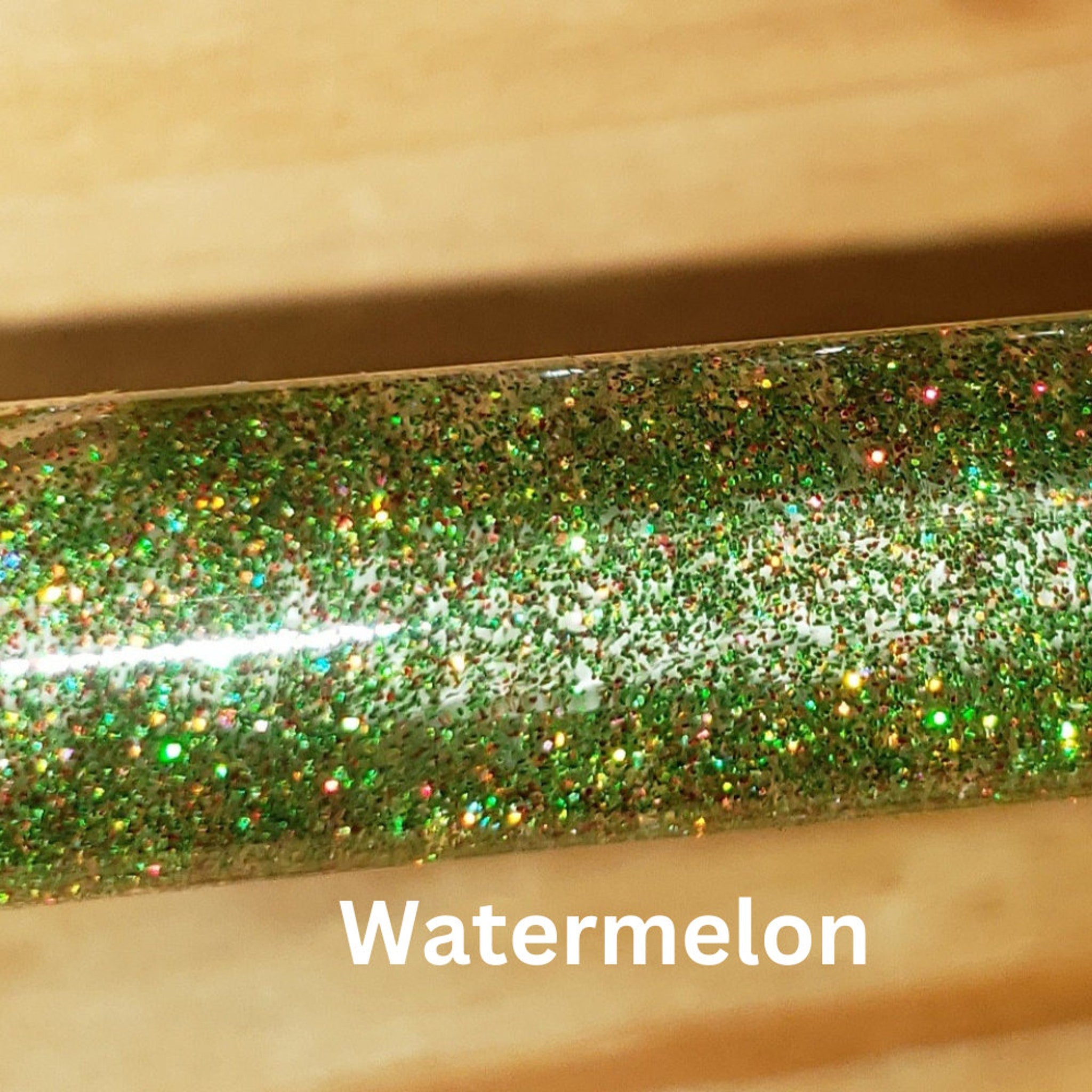 Green glitter with Watermelon text, clear tube with green glitter and small colorful specks, on wood surface