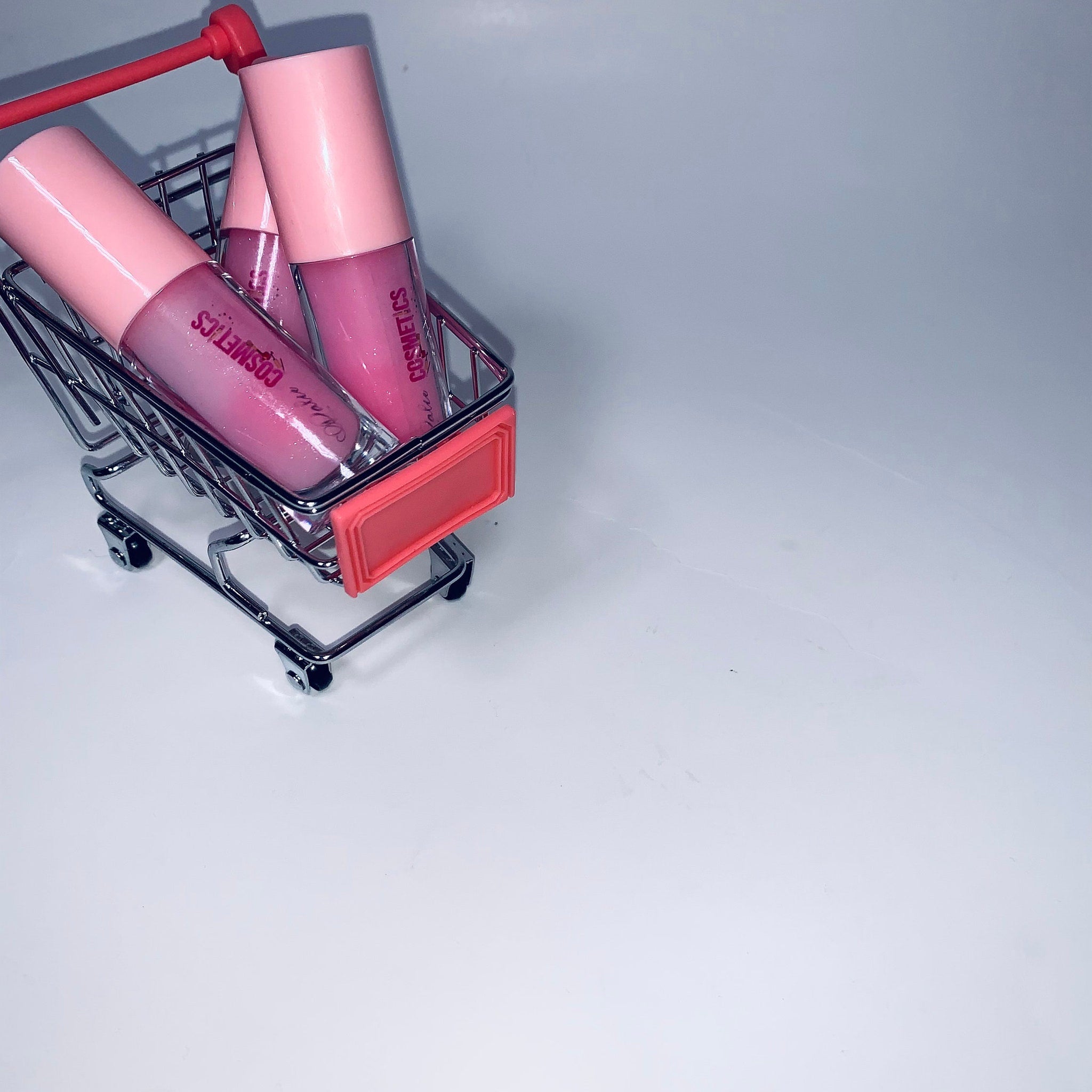 Lip gloss tubes with pink lids and clear tubes in a miniature shopping cart, "Lattia Cosmetics" visible