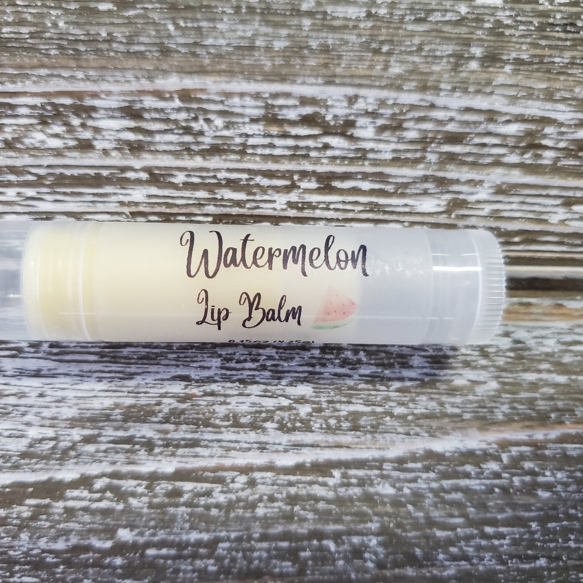 Watermelon lip balm in clear tube with black text on wooden background