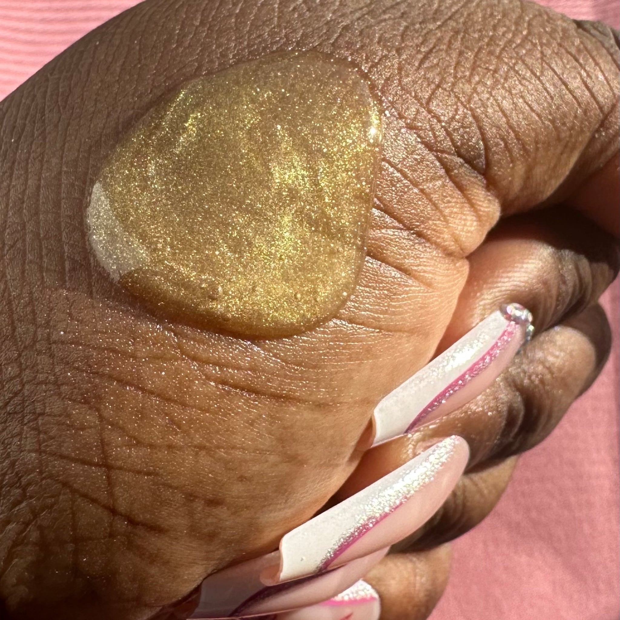 Gold glitter liquid on skin, visible hand and long white and pink nails