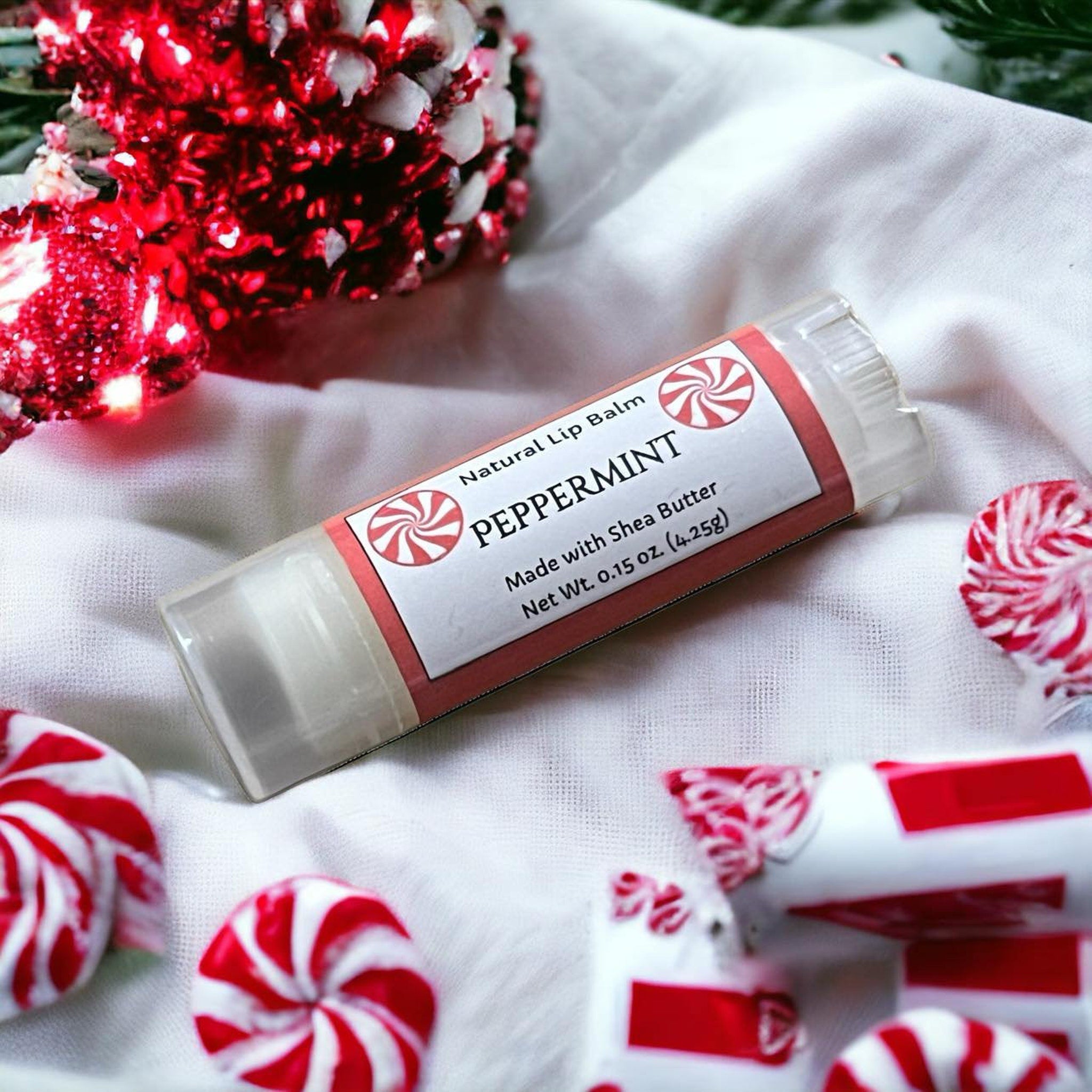 Peppermint lip balm tube with red and white label, clear tube, and peppermint candies on white fabric