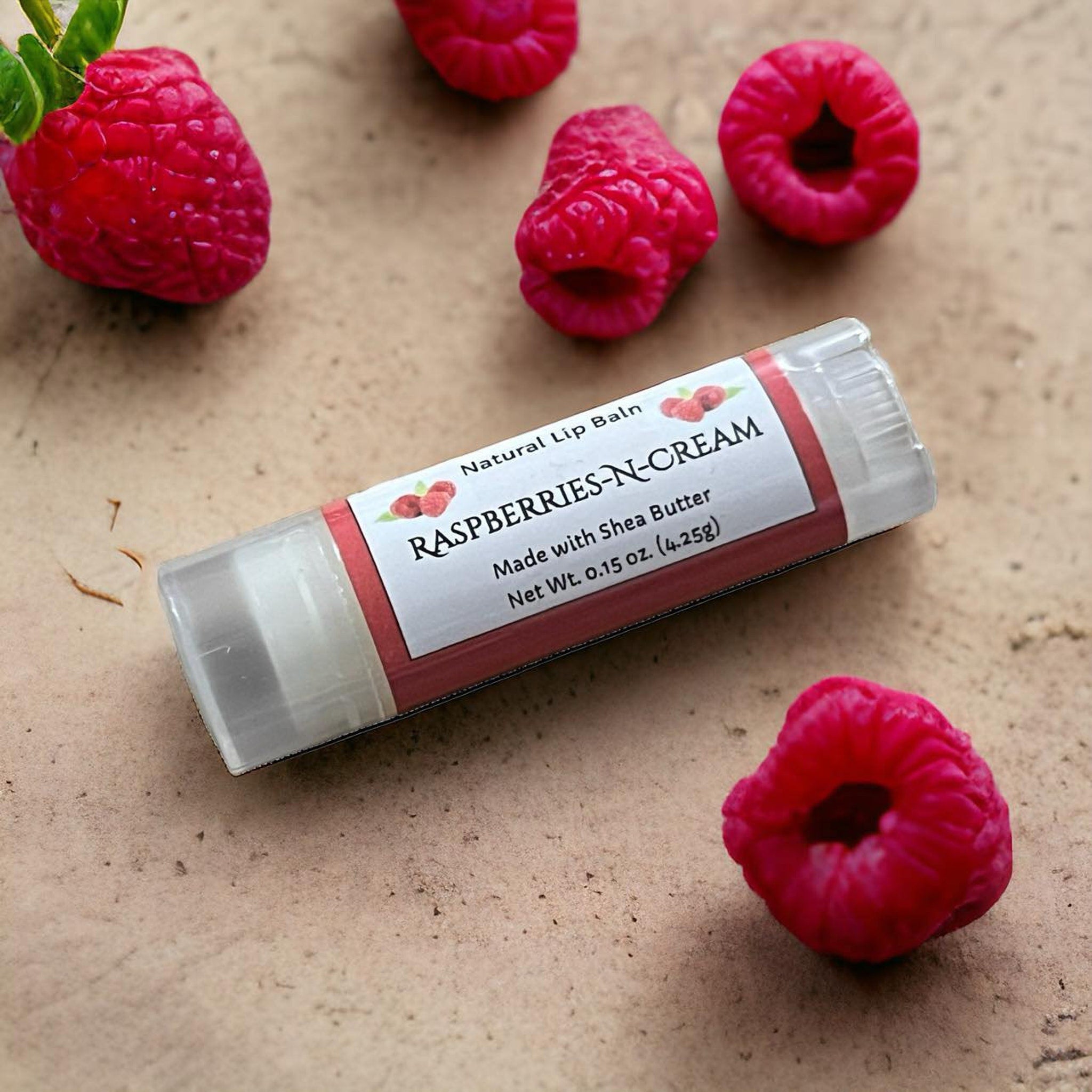 Lip balm tube with white label, red accents, and clear plastic casing, with raspberries around it