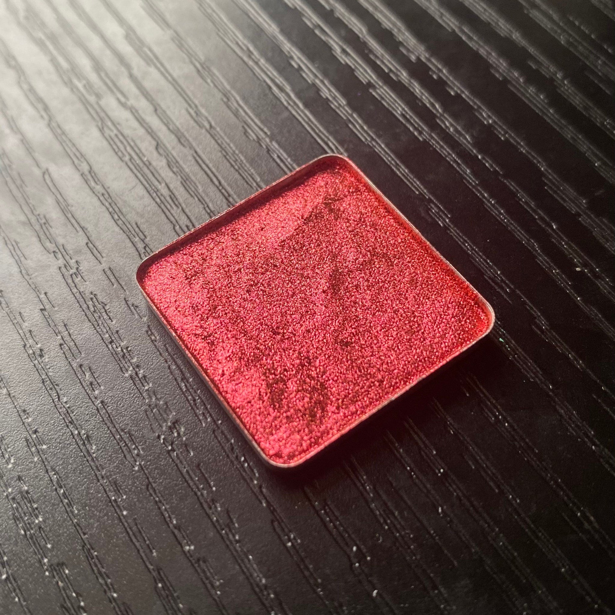Square compact with reflective black case showcasing multichrome Rubrum eye shadow pan inside