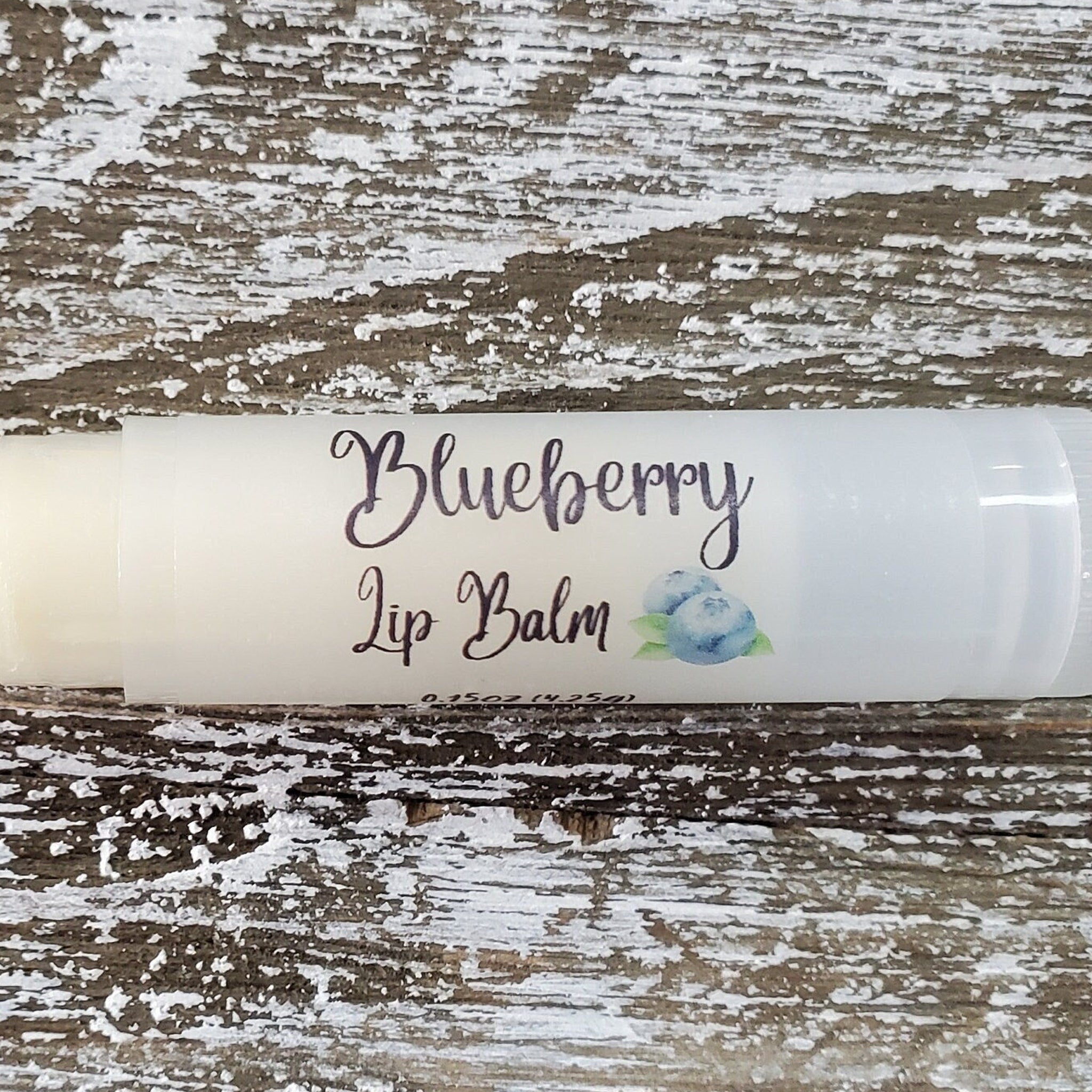 Lip balm tube with white label, "Blueberry Lip Balm" text, and blueberry illustration on wood background