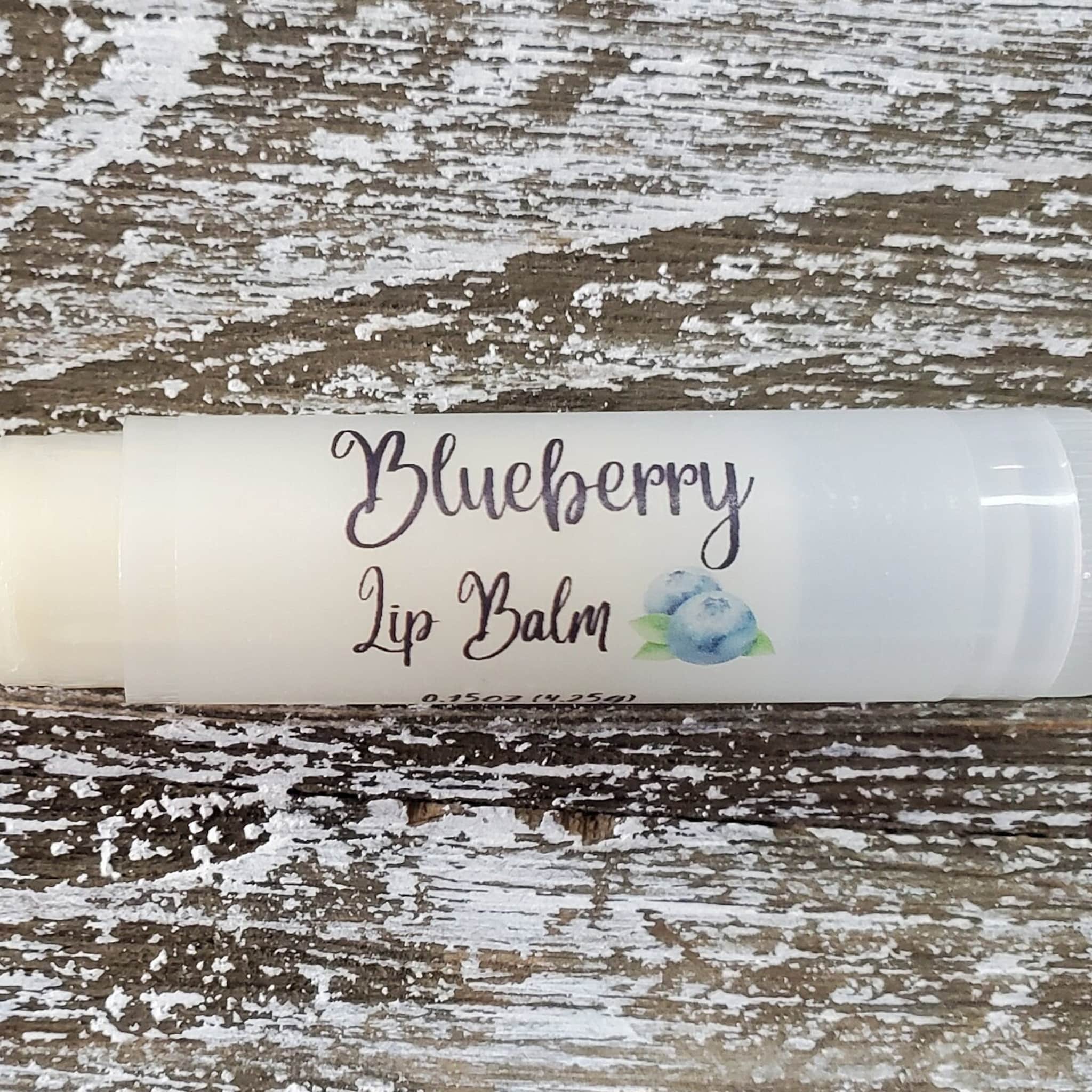 Lip balm tube with white label and blueberry graphic, on distressed wood background