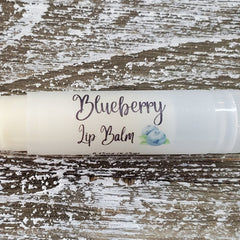 Blueberry lip balm in white tube with script text and blueberry graphic on wood background