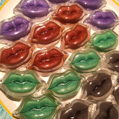 Lip-shaped glitter lip gloss in purple, red, green, and black colors, in clear plastic packaging