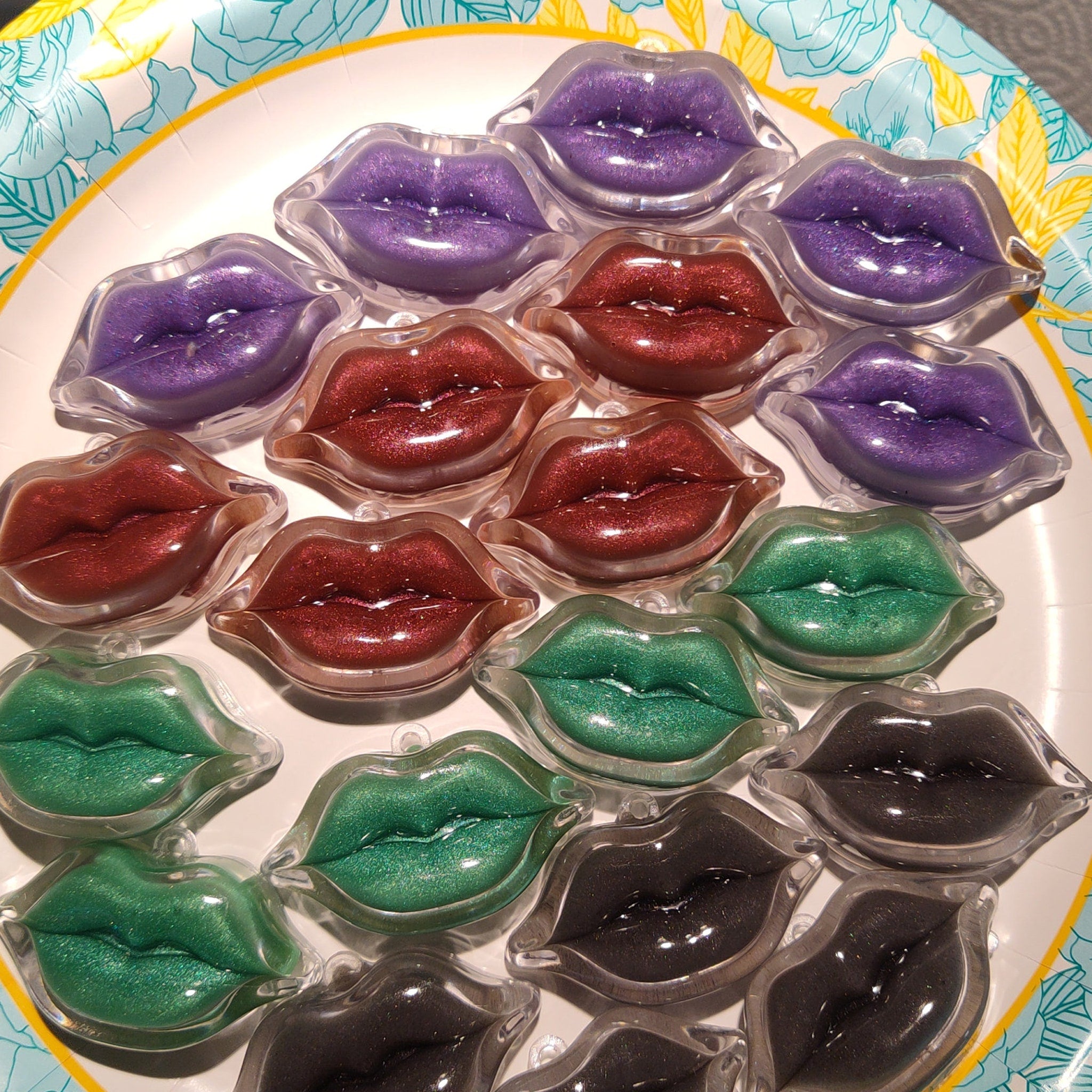 Lip-shaped lip glosses in various colors, with clear plastic containers, arranged on a plate