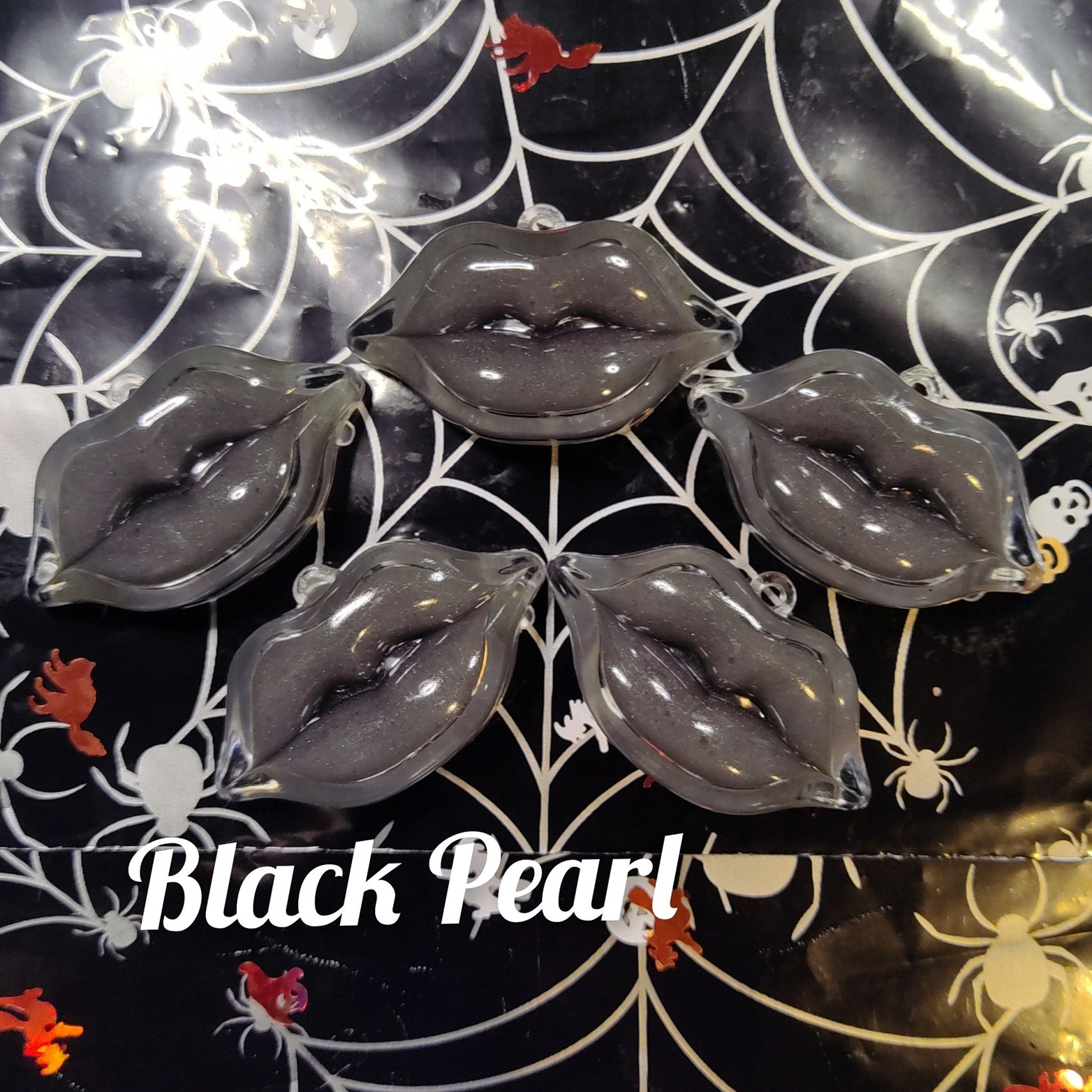 Black lip-shaped ornaments with clear loop, black glitter, on spiderweb background, Black Pearl text